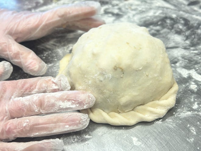 Hands crimp the edge of a freshly formed pasty.
